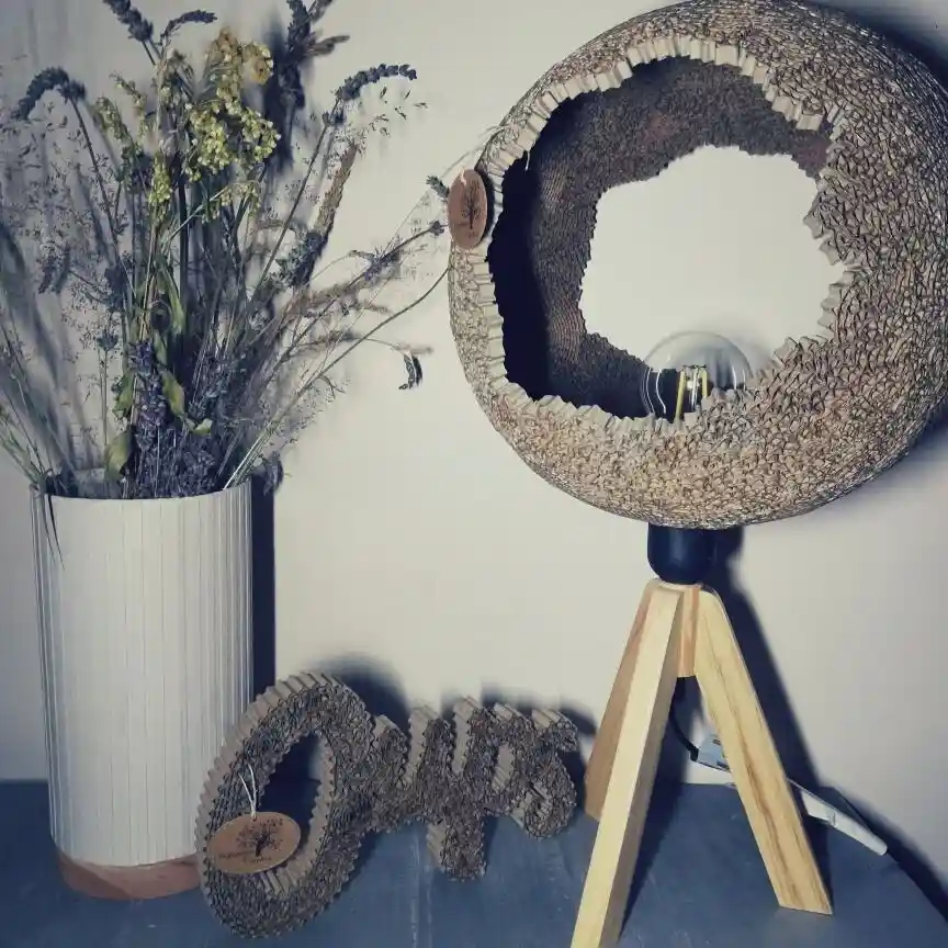 Luminaire trépied et abat-jour en dentelle de carton forme boule. Mot oups en dentelle de carton. Mis en scène sur un meuble en carton.